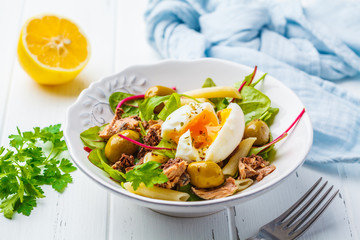 Tuna salad with pasta, olives and poached egg in white plate on white wooden background.