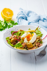 Tuna salad with pasta, olives and poached egg in white plate on white wooden background.