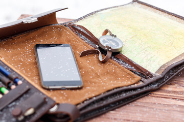 military bag. compass map and mobile phone. on the wooden background there is natural snow. there is toning