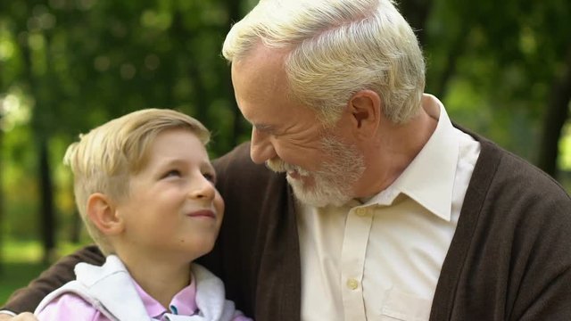 Cute boy giving high five to his old grandfather while they having rest in park
