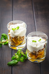 Greek yogurt mango granola parfait in a glass on dark wooden background.