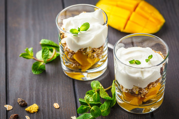 Greek yogurt mango granola parfait in a glass on dark wooden background.