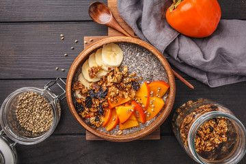 Chia pudding with banana, persimmon and granola, dark wooden background, top view, copy space.