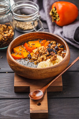 Chia pudding with banana, persimmon and granola, dark wooden background.