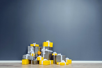A pile of yellow and grey Christmas gifts with ribbons against the wall on a beautiful hardwood floor with copyspace