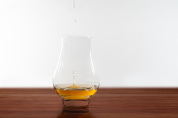 Drops of water being added to a glass of whisky, on polished wood surface