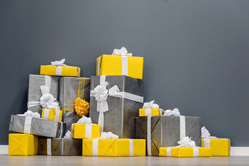 A pile of yellow and grey Christmas gifts with ribbons against the wall on a beautiful hardwood floor with copyspace