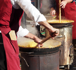 Two cooks cook polenta in the traditional way of north east italy on small wood-fired cookers