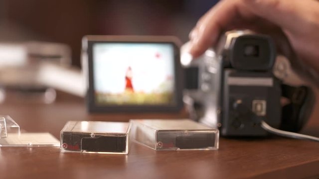 Man watching family home video on LCD screen of digital Mini DV camcorder. Young woman in summer on display of obsolete miniDV video camera.