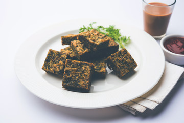 A savory cilantro cake or kothimbir vadi in square shape which is first steamed and then fried until crisp. popular indian snack served with hot tea and tomato ketchup