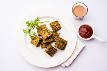 A savory cilantro cake or kothimbir vadi in square shape which is first steamed and then fried until crisp. popular indian snack served with hot tea and tomato ketchup