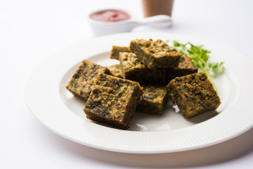 A savory cilantro cake or kothimbir vadi in square shape which is first steamed and then fried until crisp. popular indian snack served with hot tea and tomato ketchup