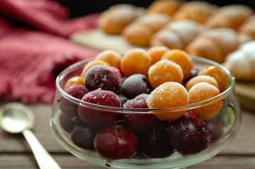 Frozen cherries and cherry plums in a glass dish against the background of fresh baked croissants on a wooden stand.