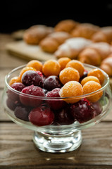 Frozen cherries and cherry plums in a glass dish against the background of fresh baked croissants on a wooden stand.