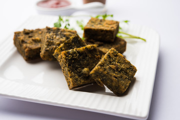 A savory cilantro cake or kothimbir vadi in square shape which is first steamed and then fried until crisp. popular indian snack served with hot tea and tomato ketchup