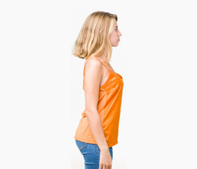 Beautiful young woman wearing orange shirt over isolated background looking to side, relax profile pose with natural face with confident smile.