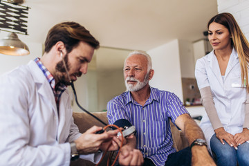 Nurse measuring blood pressure of senior man at home. Smiling to each other. Home care.