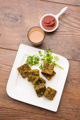 A savory cilantro cake or kothimbir vadi in square shape which is first steamed and then fried until crisp. popular indian snack served with hot tea and tomato ketchup