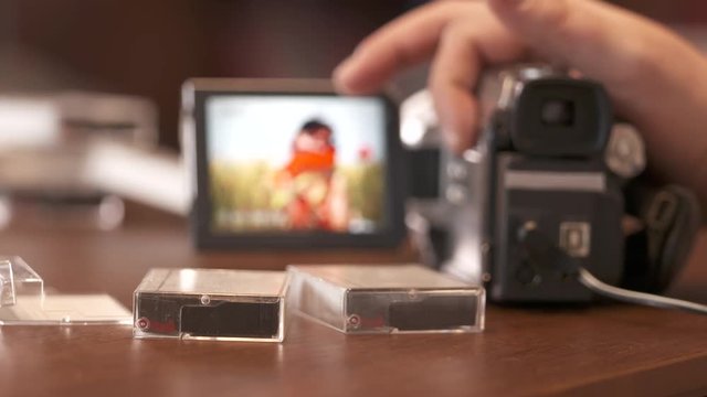 Man watching family home video on LCD screen of digital Mini DV camcorder. Young woman in summer on display of obsolete miniDV video camera.