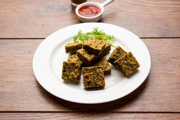 A savory cilantro cake or kothimbir vadi in square shape which is first steamed and then fried until crisp. popular indian snack served with hot tea and tomato ketchup