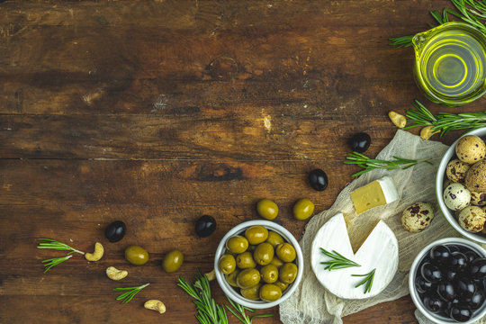 Cheese camembert, black and green olives, quail eggs on plates, olive oil and rosemary, cashew nuts