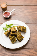 A savory cilantro cake or kothimbir vadi in square shape which is first steamed and then fried until crisp. popular indian snack served with hot tea and tomato ketchup