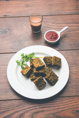 A savory cilantro cake or kothimbir vadi in square shape which is first steamed and then fried until crisp. popular indian snack served with hot tea and tomato ketchup