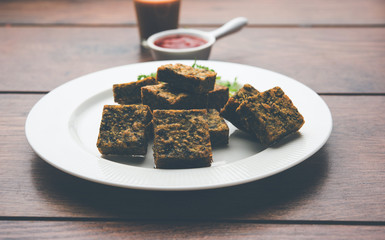 A savory cilantro cake or kothimbir vadi in square shape which is first steamed and then fried until crisp. popular indian snack served with hot tea and tomato ketchup