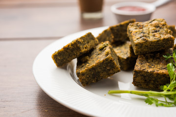 A savory cilantro cake or kothimbir vadi in square shape which is first steamed and then fried until crisp. popular indian snack served with hot tea and tomato ketchup