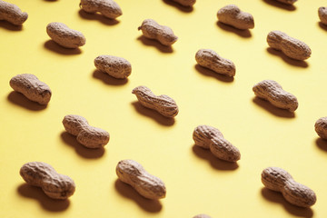 close-up peanuts in shells arranged in endless rows on yellow paper background - selective focus