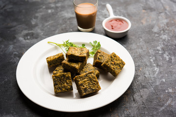 A savory cilantro cake or kothimbir vadi in square shape which is first steamed and then fried until crisp. popular indian snack served with hot tea and tomato ketchup