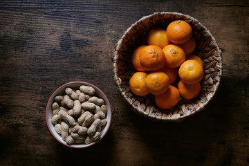 overhead top view of two bowls full of peanut nuts and clementine mandarin ornages on rustic wooden table