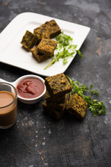 A savory cilantro cake or kothimbir vadi in square shape which is first steamed and then fried until crisp. popular indian snack served with hot tea and tomato ketchup