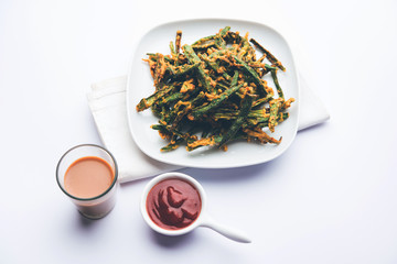 Kurkuri bhindi or crispy ladyfinger or okra fry recipe, served in a bowl with ketchup and hot tea. selective focus