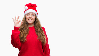Young blonde woman wearing santa claus hat doing ok sign with fingers, excellent symbol
