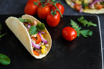 Mexican tacos with pork, vegetables and spices on a black stone plate on a dark background with ingredients for tacos