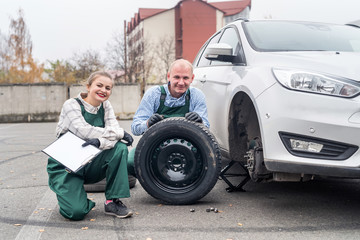 Fototapeta na wymiar Two mechanics at car service with spare wheel