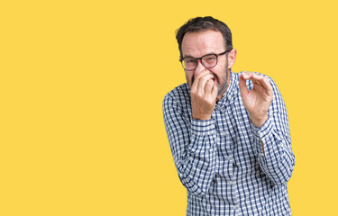 Naklejka premium Handsome middle age elegant senior business man wearing glasses over isolated background smelling something stinky and disgusting, intolerable smell, holding breath with fingers on nose