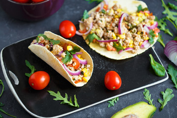 Mexican tacos with pork, vegetables and spices on a black stone plate on a dark background with ingredients for tacos