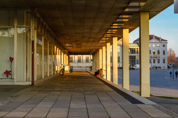 Exterior diminishing perspective view of people sit on stair at arcade, covered way, of old modern shabby student dormitory at Am Alten Markt in Potsdam, Germany.