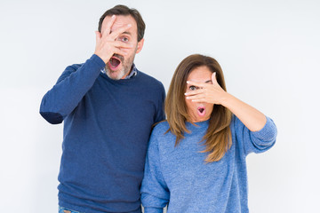 Beautiful middle age couple in love over isolated background peeking in shock covering face and eyes with hand, looking through fingers with embarrassed expression.