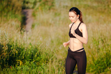 Naklejka na ściany i meble young sports woman engaged in the summer morning running in the Park. in the headphones listening to music from your phone. concept of a healthy lifestyle