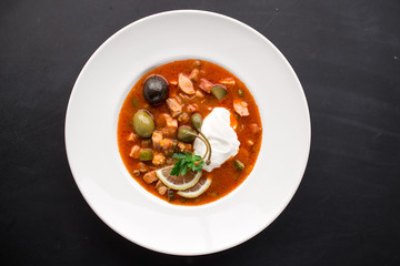 Traditional Russian soup Solyanka made from cabbage with olives, lemon and capers on black background