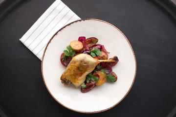 Duck leg confit with potatoes and plum on black background