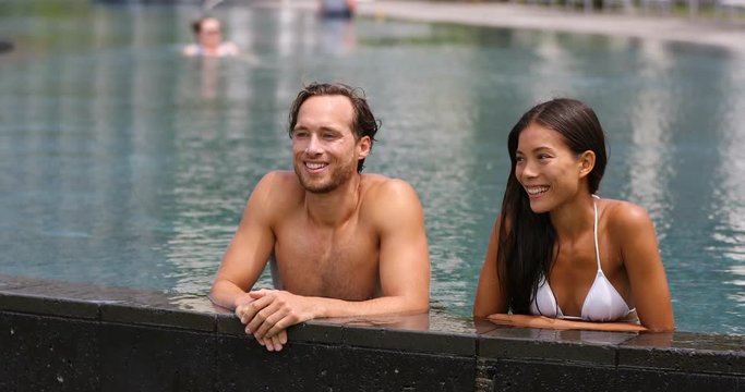 Couple relaxing together in swimming pool in luxury resort hotel vacation retreat at beach destination. Luxurious hotel travel vacation. People relaxed enjoying summer holidays. 59.94 FPS.