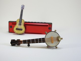 A miniature banjo and a miniature acoustic guitar propped up on a red 10-hole diatonic harmonica....