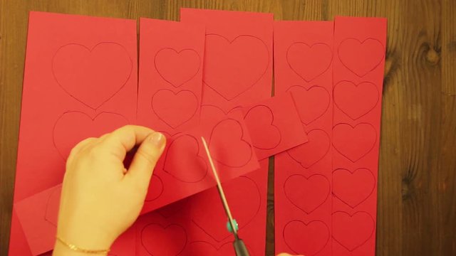 The girl cuts blanks of hearts from red cardboard. Close-up