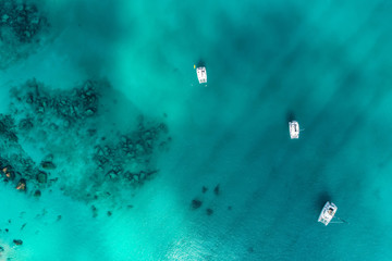 Fototapeta premium Spectacular aerial view of some yachts and small boats floating on a clear and turquoise sea, Seychelles in the Indian Ocean.Top view from drone