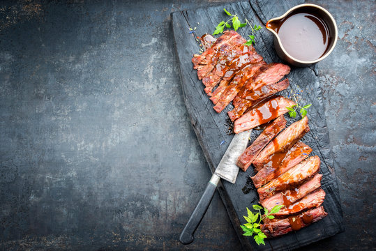 Traditional American barbecue dry aged flank steak sliced with hot sauce and chili as top view on an old carbonized board with copy space left