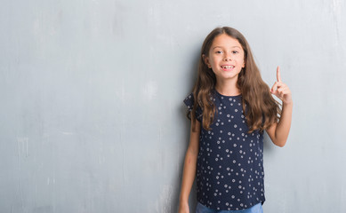 Young hispanic kid over grunge grey wall showing and pointing up with finger number one while smiling confident and happy.